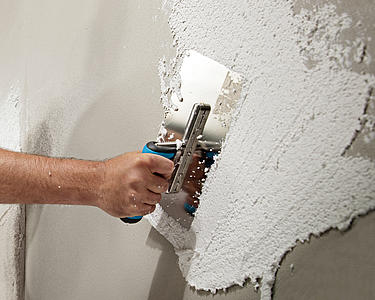 [Translate to Latvian:] Hand mit Kelle verputzt eine Wand